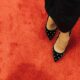 Black high heel shoes with studded design on vibrant red carpet. Fashion statement.