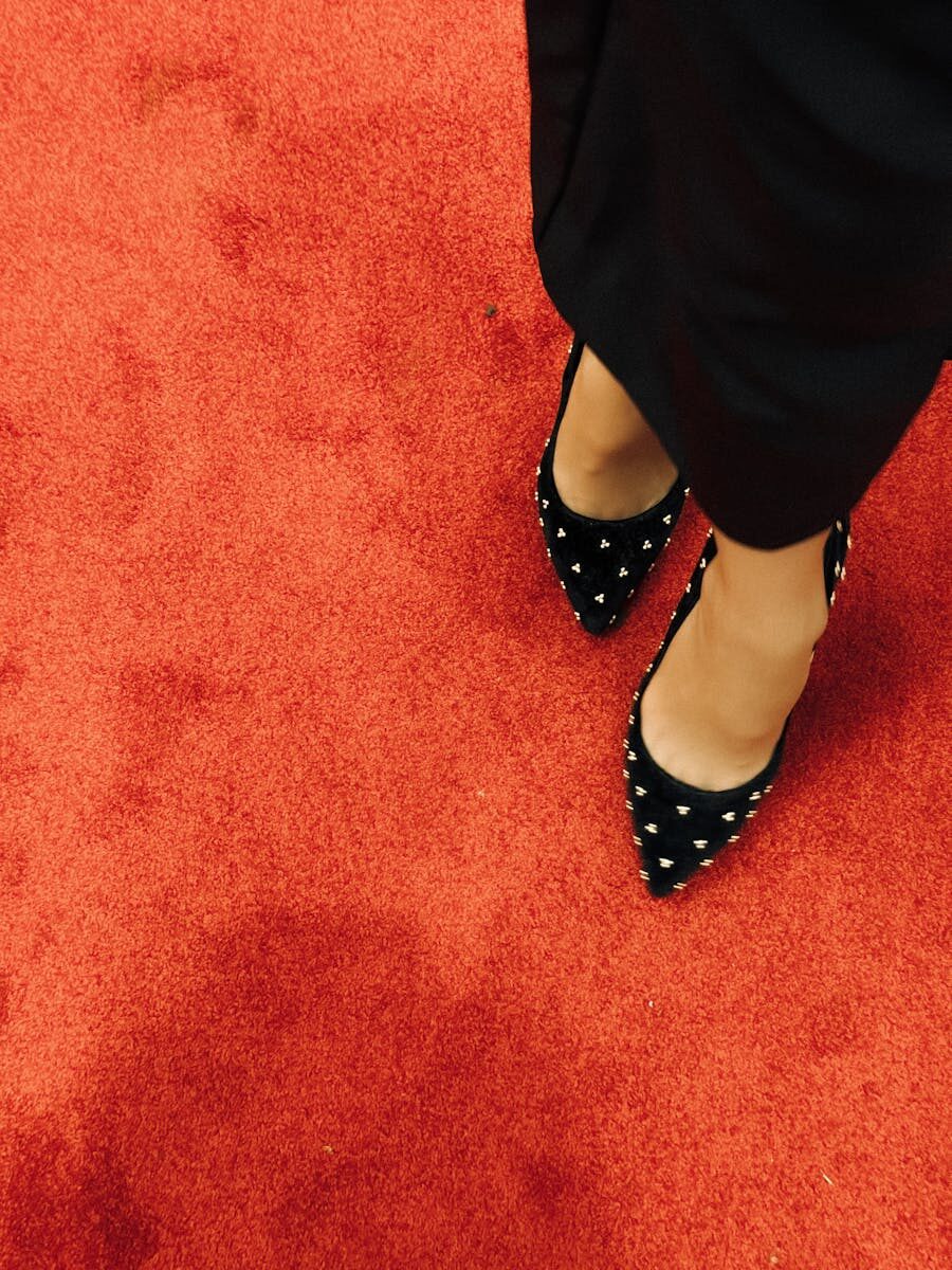 Black high heel shoes with studded design on vibrant red carpet. Fashion statement.