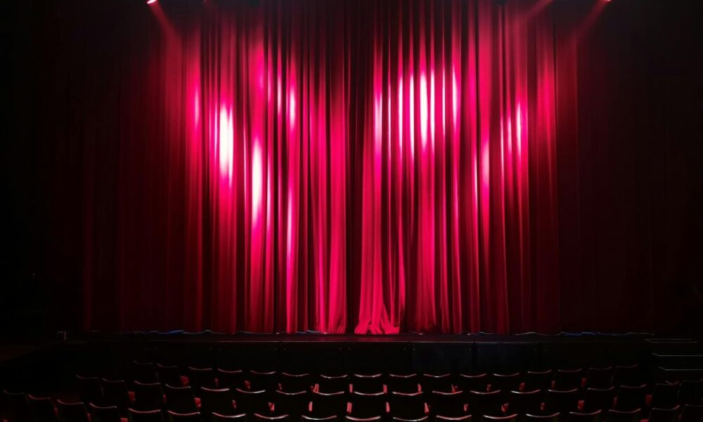 Empty theater stage with red curtains and seating, ready for a performance.