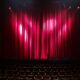 Empty theater stage with red curtains and seating, ready for a performance.