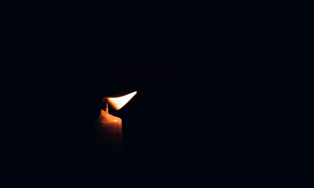 A single burning candle illuminates the darkness, casting a warm glow.