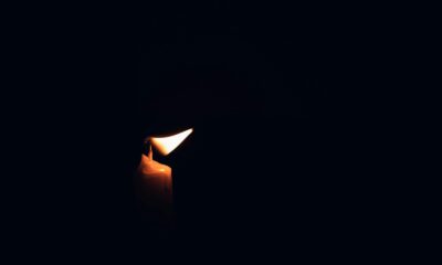 A single burning candle illuminates the darkness, casting a warm glow.