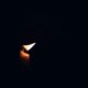 A single burning candle illuminates the darkness, casting a warm glow.