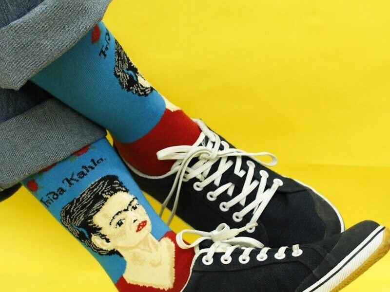 Stylish artistic socks featuring Frida Kahlo design with black sneakers on a vibrant yellow background.