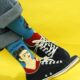 Stylish artistic socks featuring Frida Kahlo design with black sneakers on a vibrant yellow background.