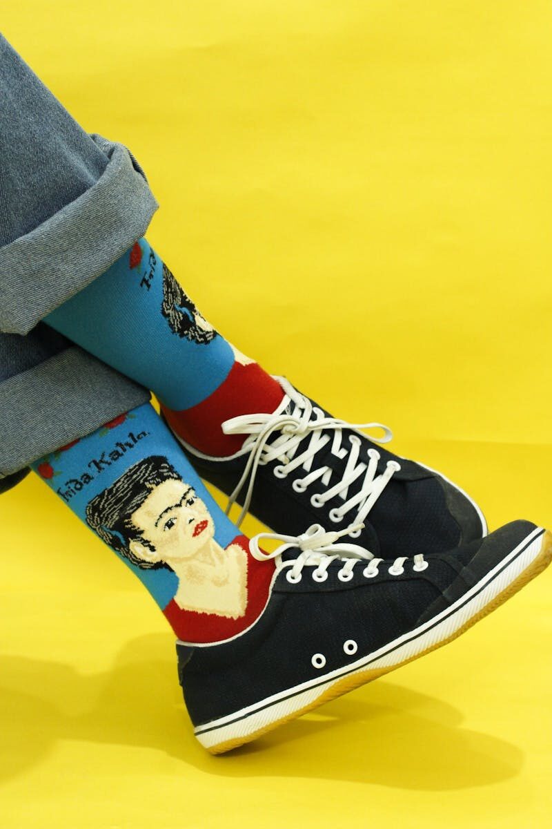 Stylish artistic socks featuring Frida Kahlo design with black sneakers on a vibrant yellow background.
