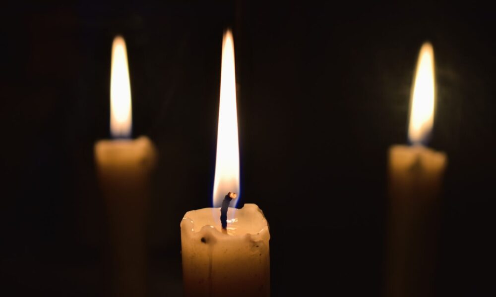 Three lit candles casting a warm glow in the darkness, creating a serene and contemplative atmosphere.