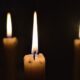 Three lit candles casting a warm glow in the darkness, creating a serene and contemplative atmosphere.