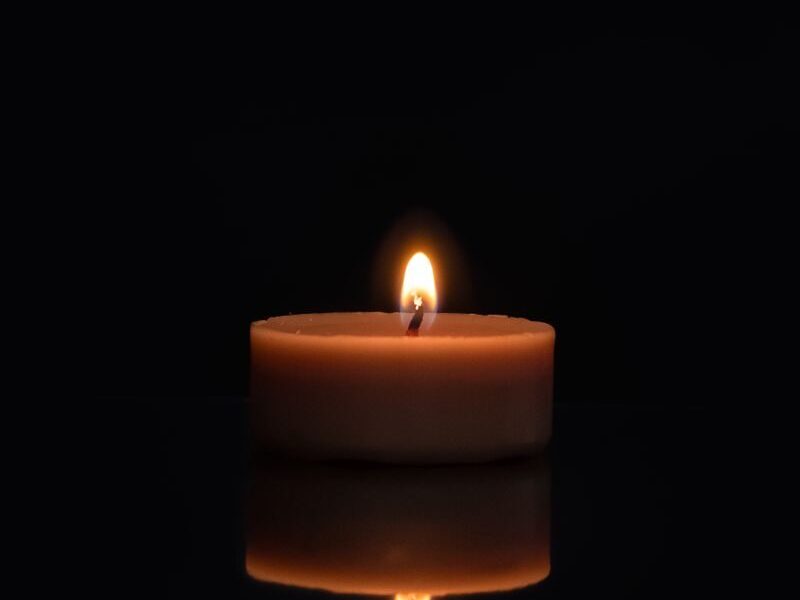 A single candle flame reflecting on a dark surface with a black background.
