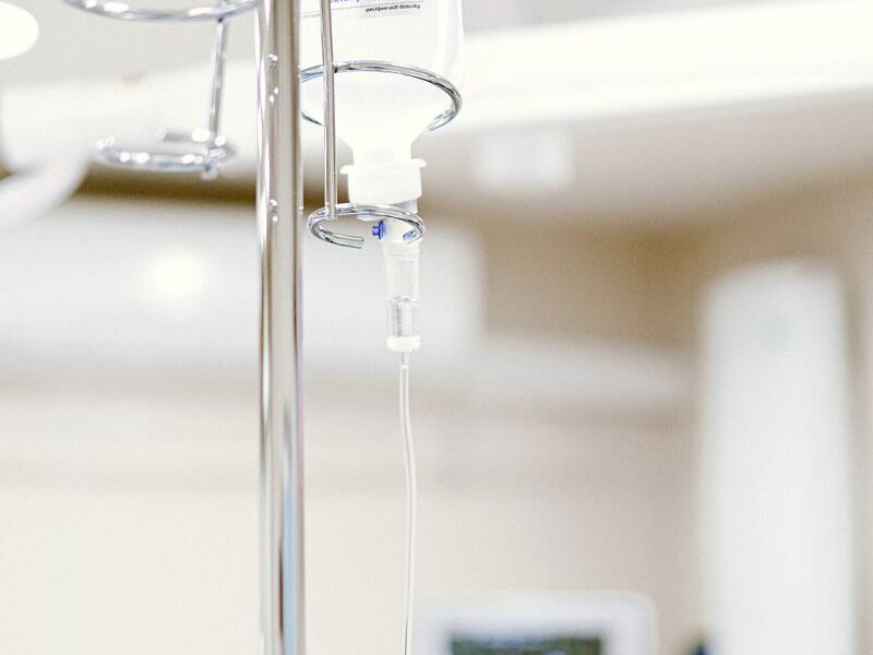Close-up of an IV drip in a sterile hospital setting with background medical equipment.