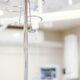 Close-up of an IV drip in a sterile hospital setting with background medical equipment.